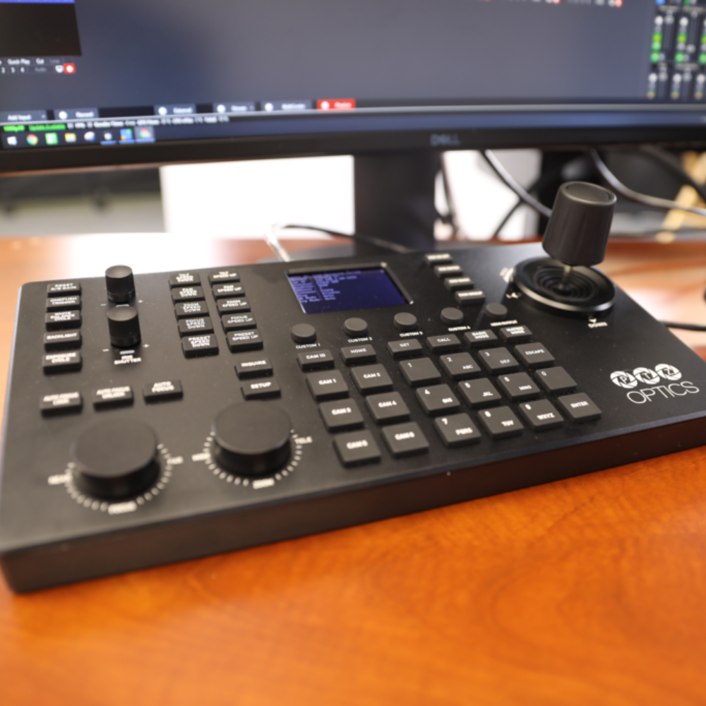 PTZOptics Superjoy IP & Serial PTZ Camera Joystick Controller Control panel with buttons and displays on a wooden surface, featuring the brand 'PTZOptics'.