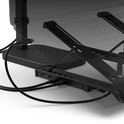 Black metal monitor arm and dock with multiple USB-C ports, shown in a close-up studio-style shot with cables connected and a blurred monitor in the background.