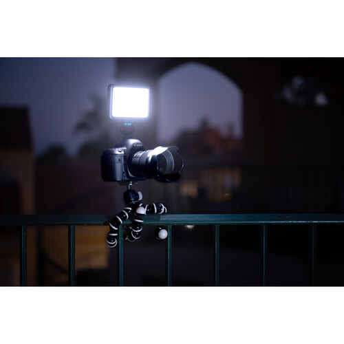 Camera on a tripod with a light attached, set against a dark outdoor background.