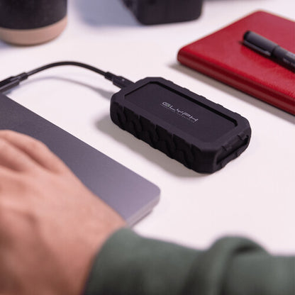Black external hard drive on a desk with a person's hand and office items in the background