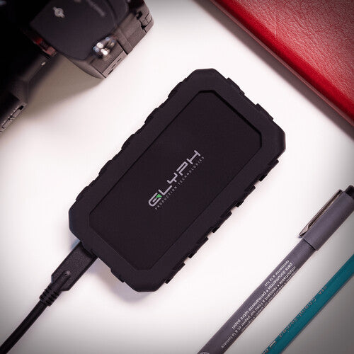 Black external hard drive with 'GLYPH' branding on a light surface with office supplies.