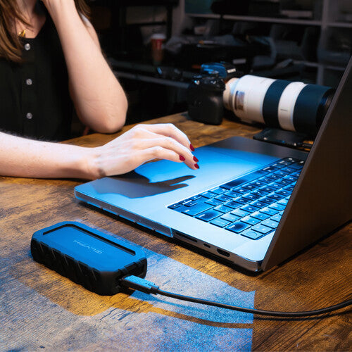 Person using a laptop with a external hard drive connected on a wooden desk.