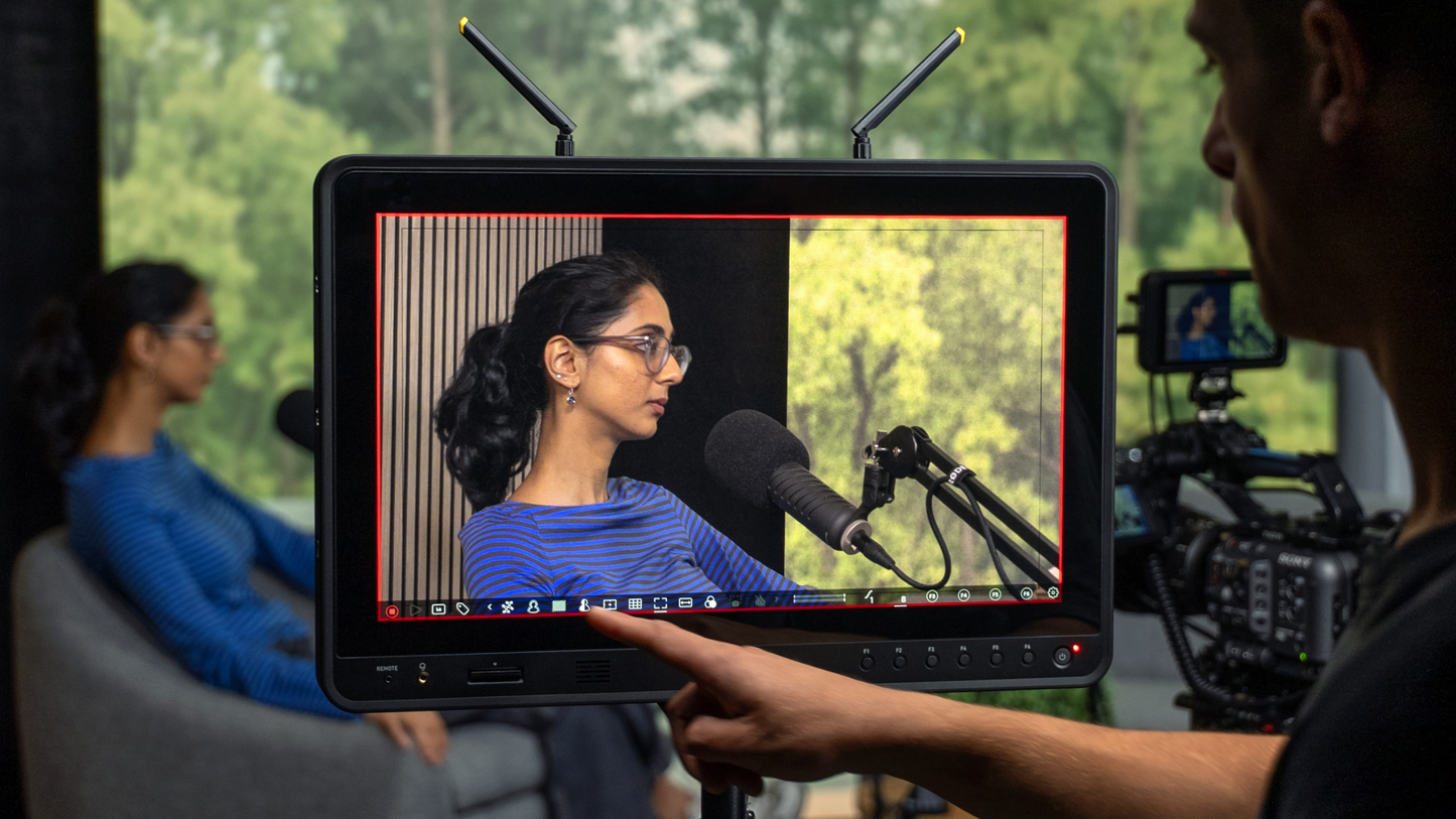 Person holding a monitor displaying a woman being interviewed outdoors
