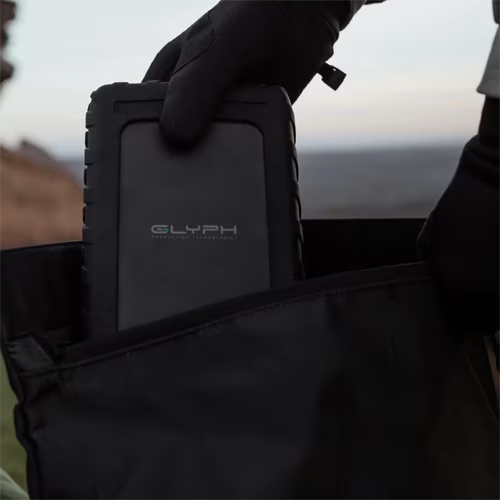 Person holding a black carrying case with 'GLYPH' branding against a blurred natural background