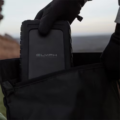 Person holding a black carrying case with 'GLYPH' branding against a blurred natural background