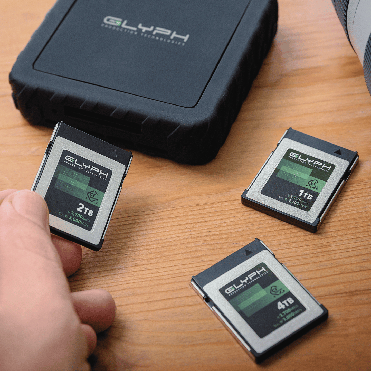Three Glyph CFexpress memory cards on a wooden surface with a hand holding one of them.