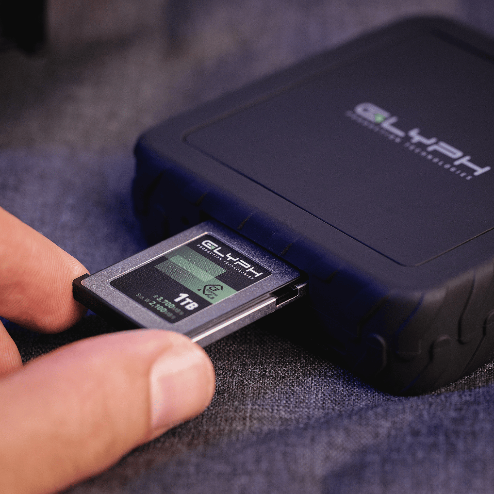 Person holding a CFexpress memory card next to a CFexpress memory card reader with 'GLYPH' branding.