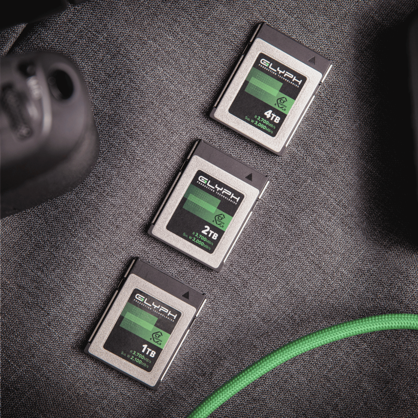 Three Glyph CFexpress memory cards of different capacities on a textured surface with a green cable.