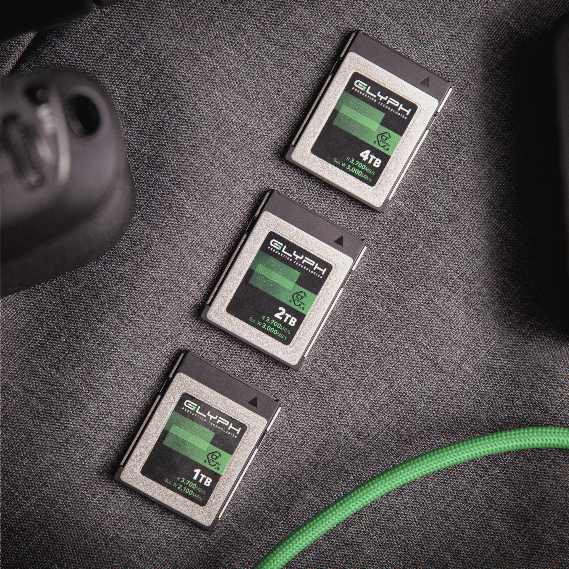 Three Glyph CFexpress memory cards of different capacities on a textured surface with a green cable.