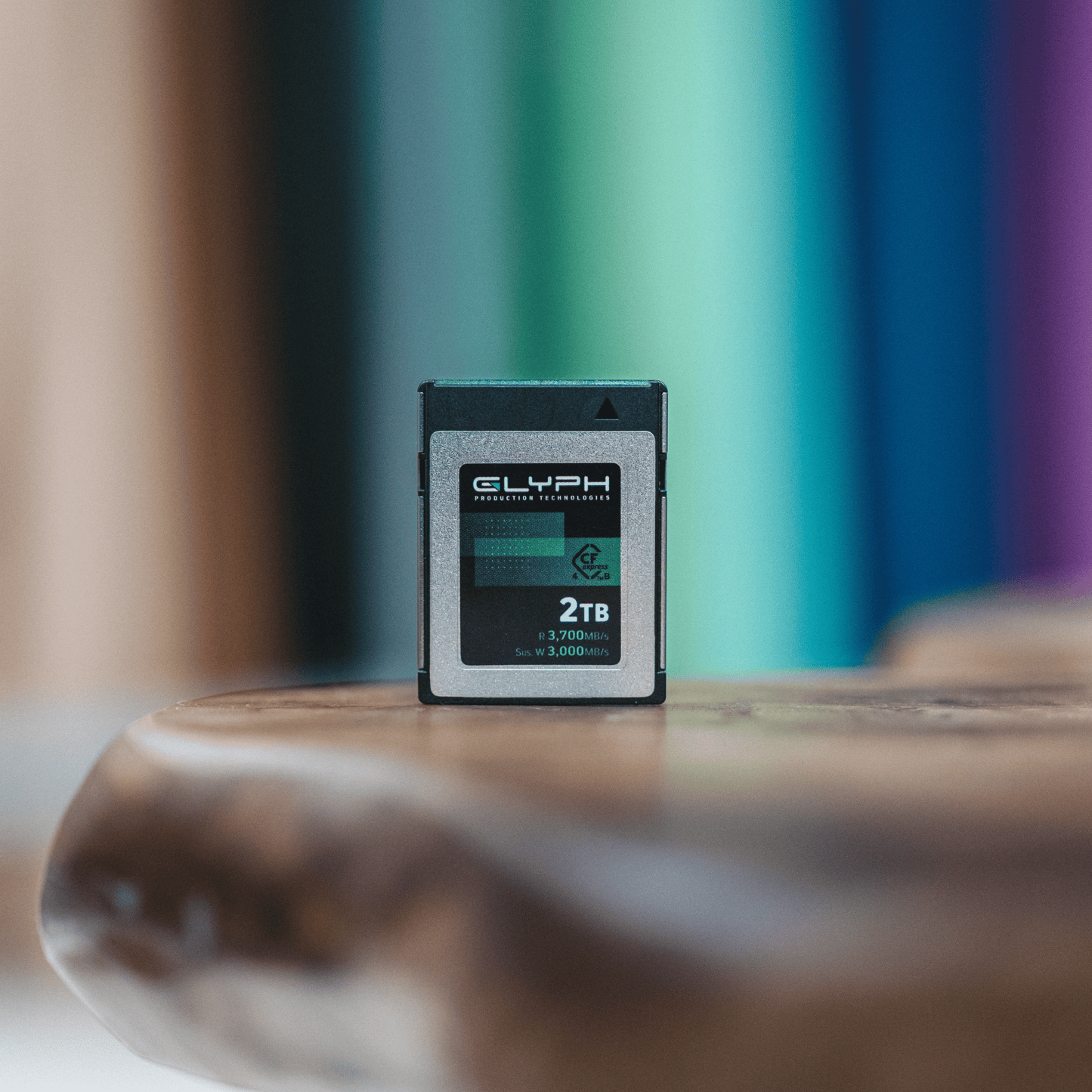 2TB Glyph CFexpress memory card on a wooden surface with a blurred colorful background