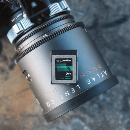 Camera lens with a Glyph 2TB memory card attached on a textured surface