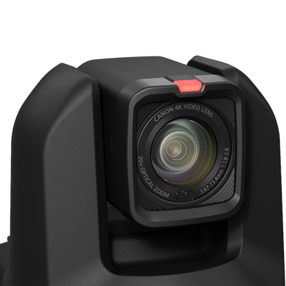 Close-up of a black Canon 4K video lens attached to a camera body, with a small red tab visible above the lens on a clean white background.