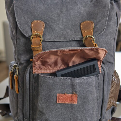 Gray backpack with brown leather straps and pocket, containing a black device.