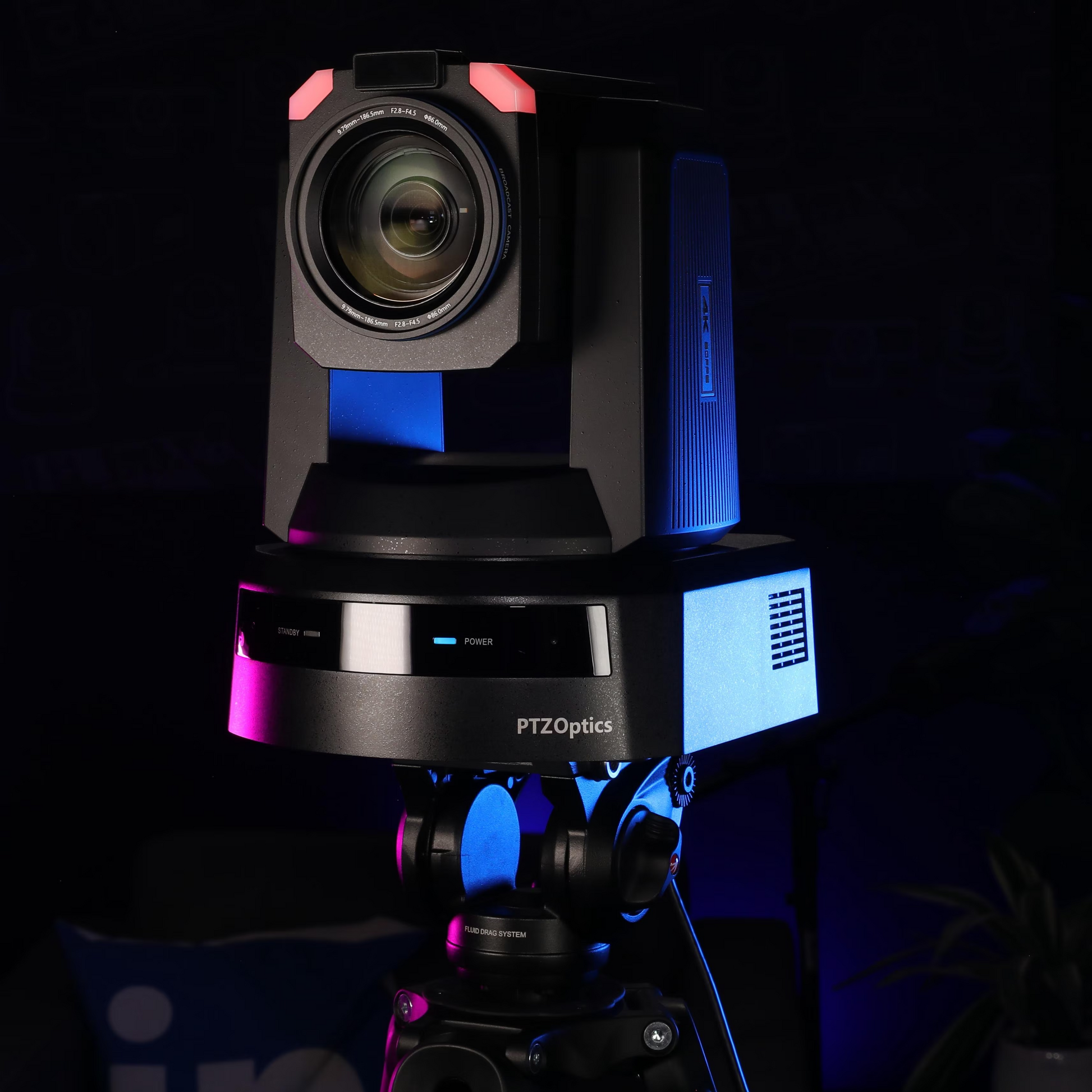 PTZOptics PTZ camera on a tripod in a dark room with blue and pink accent lighting.