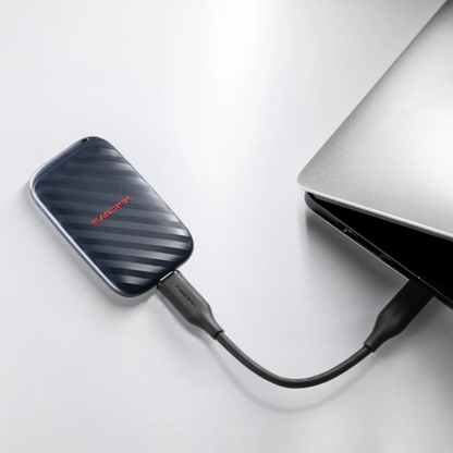 A black external hard drive with a red 'SANDISK' logo, connected via a black USB cable to a silver laptop on a clean white surface.