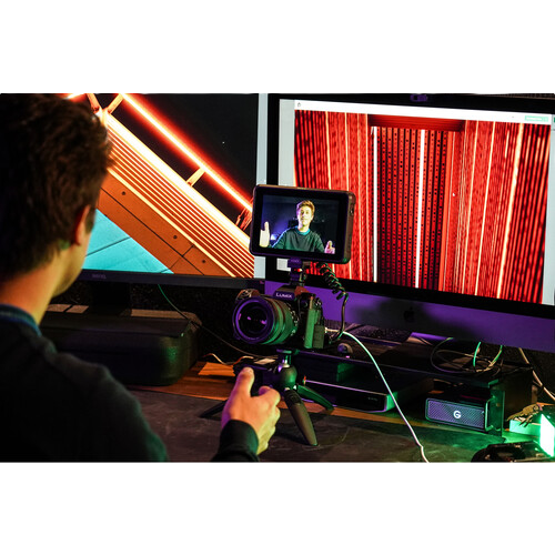 Person using a camera on a tripod with two monitors displaying different scenes.