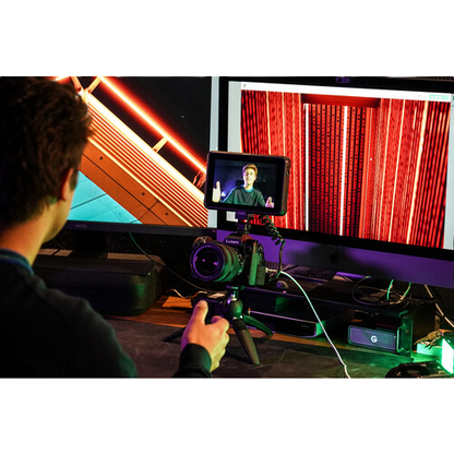 Person using a camera on a tripod with two monitors displaying different scenes.